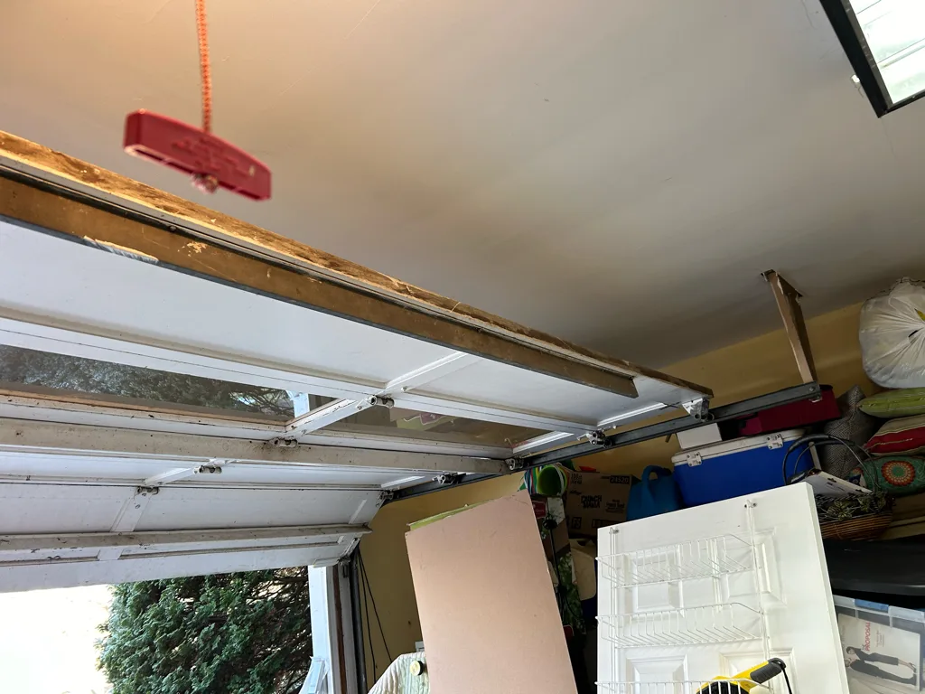 The header and horizontal tracks above an open garage door, with the red emergency release handle hanging from the trolley on its cord.